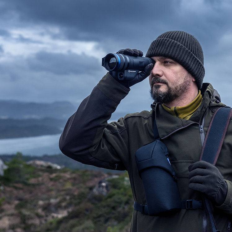 Man using Pulsar Telos XP50 thermal monocular in rugged terrain, demonstrating ergonomic grip and field usability.