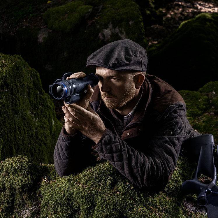 Man aiming Pulsar Telos XQ35 LRF thermal monocular in mossy forest, emphasizing its precision optics and tactical usability.