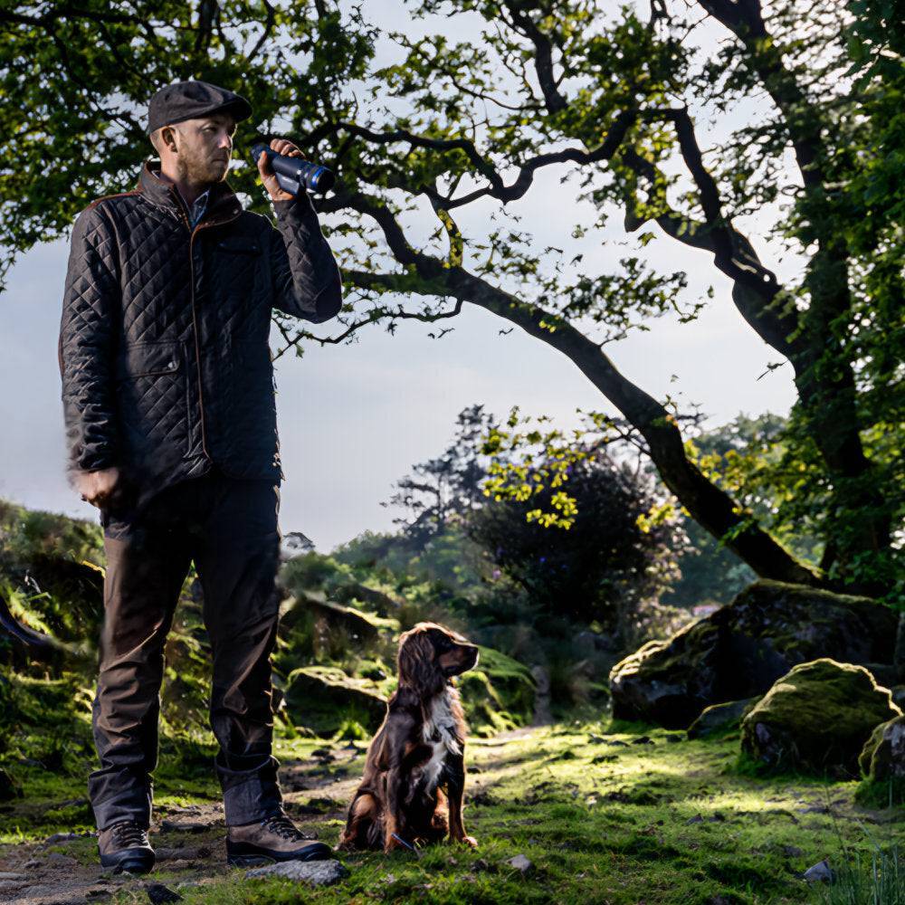 Hunter with dog using Pulsar Telos XQ35 LRF thermal monocular in forest, ideal for wildlife tracking and outdoor exploration.